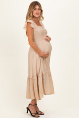 woman wearing a beige maternity dress with ruffle sleeves and a smocked bodice, showcasing her baby bump