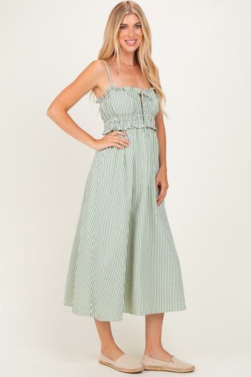 woman wearing a green and white striped midi dress with spaghetti straps and a ruffled bodice, standing in a relaxed pose