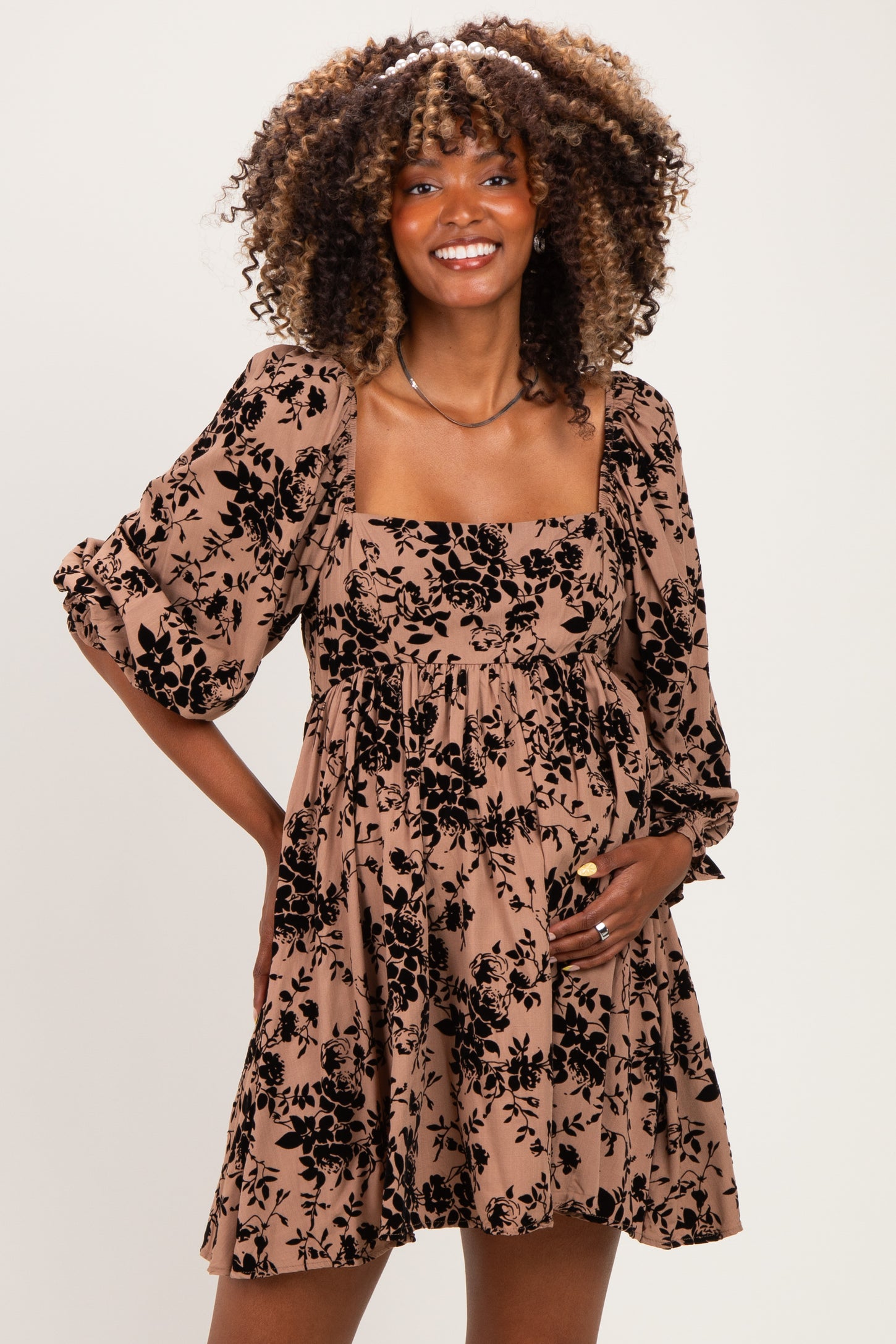 woman wearing a brown floral maternity dress with puff sleeves and a visible baby bump