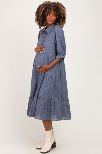 woman wearing a navy blue gingham maternity dress with puff sleeves and a tiered skirt, cradling her baby bump