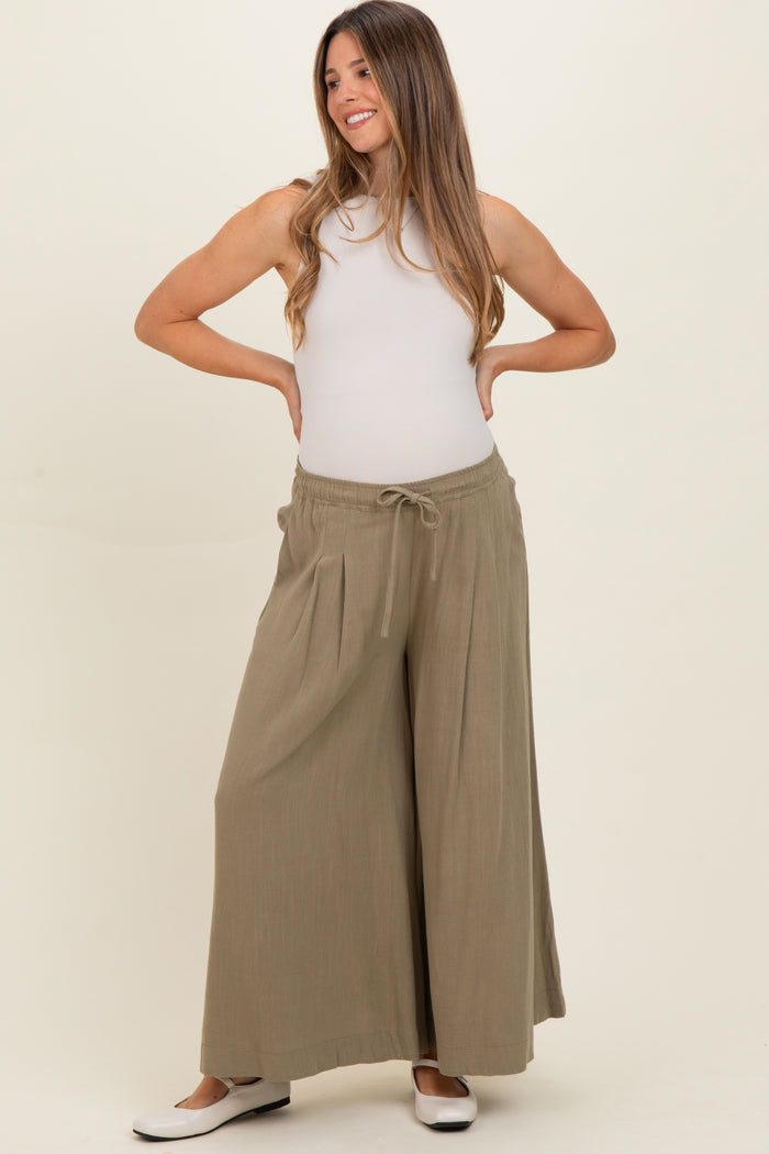 woman wearing olive green maternity wide-leg pants with a drawstring waist and a fitted white tank top, smiling with hands on hips