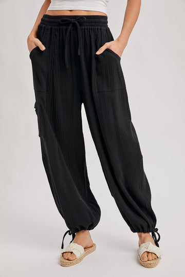 woman wearing black relaxed fit pants with pockets and drawstring hem, paired with white sandals