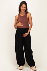 woman wearing a brown maternity tank top and black wide-leg maternity pants, holding her baby bump
