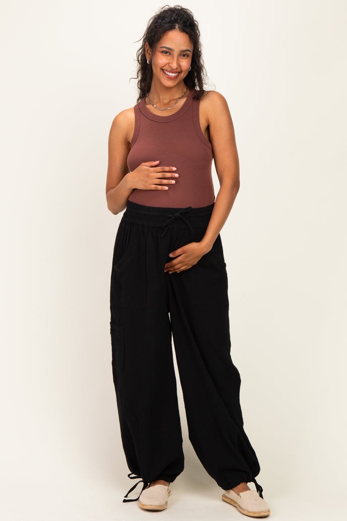 woman wearing a brown maternity tank top and black wide-leg maternity pants, holding her baby bump