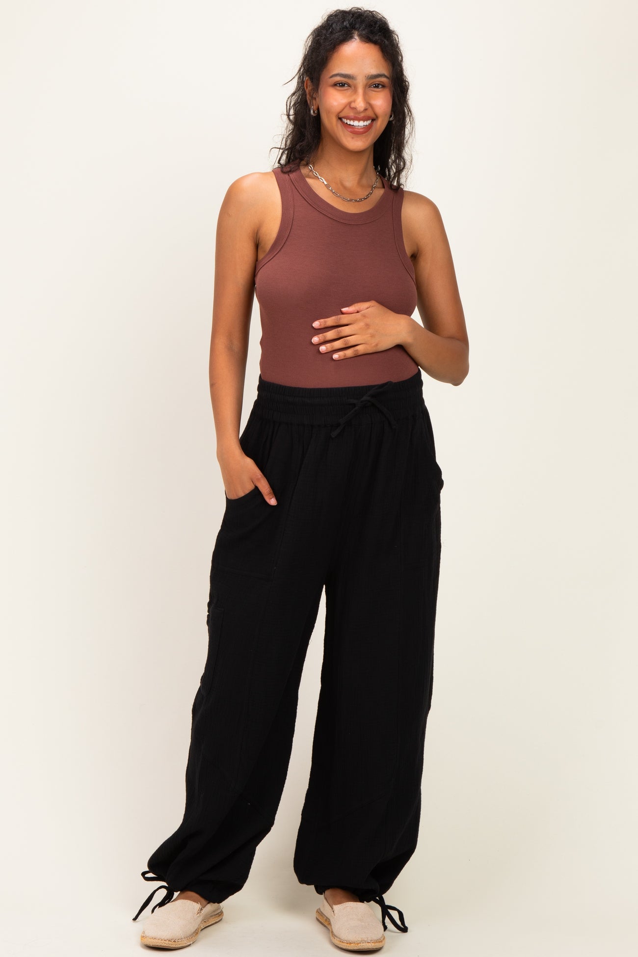 woman wearing a rust ribbed maternity tank top and black loose-fitting maternity pants, holding her baby bump