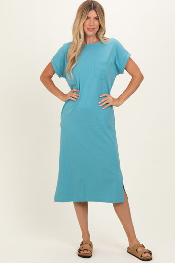 woman wearing a turquoise short sleeve maxi dress with a pocket and side slits, standing in a relaxed pose