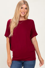 woman wearing a maroon oversized short sleeve top with a round neckline and relaxed fit paired with blue jeans