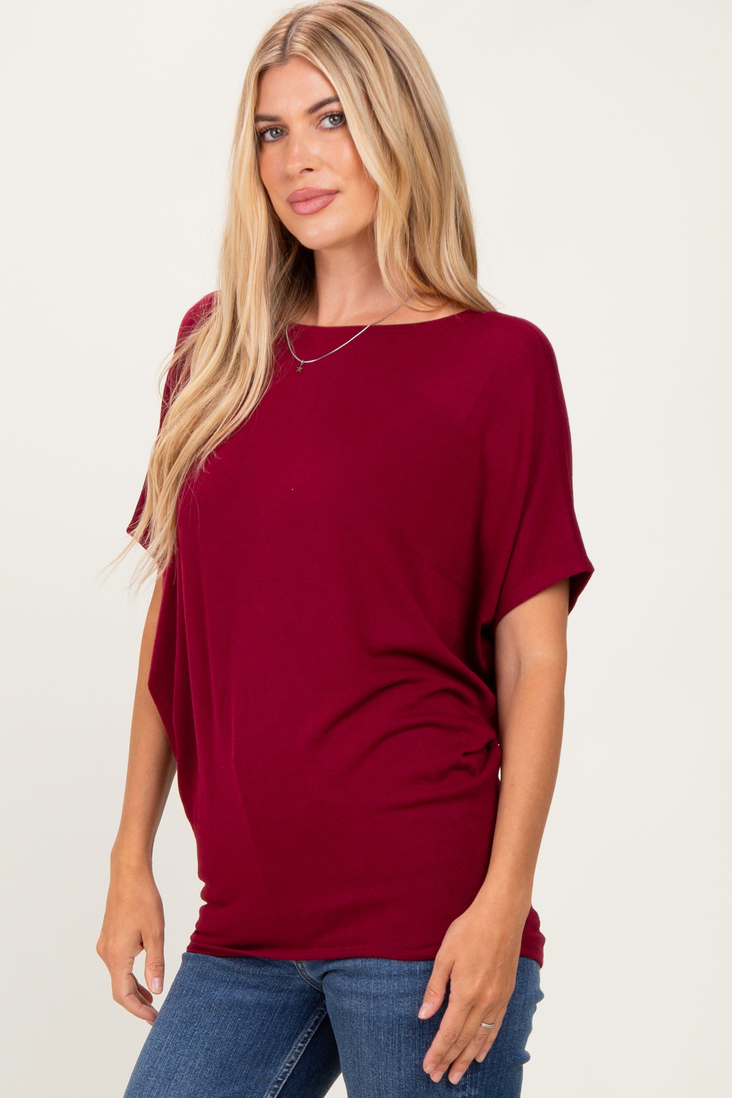 woman wearing a burgundy short sleeve top with a relaxed fit and side ruching, paired with blue jeans