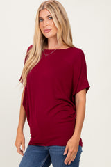 woman wearing a burgundy short sleeve top with a relaxed fit and side ruching, paired with blue jeans