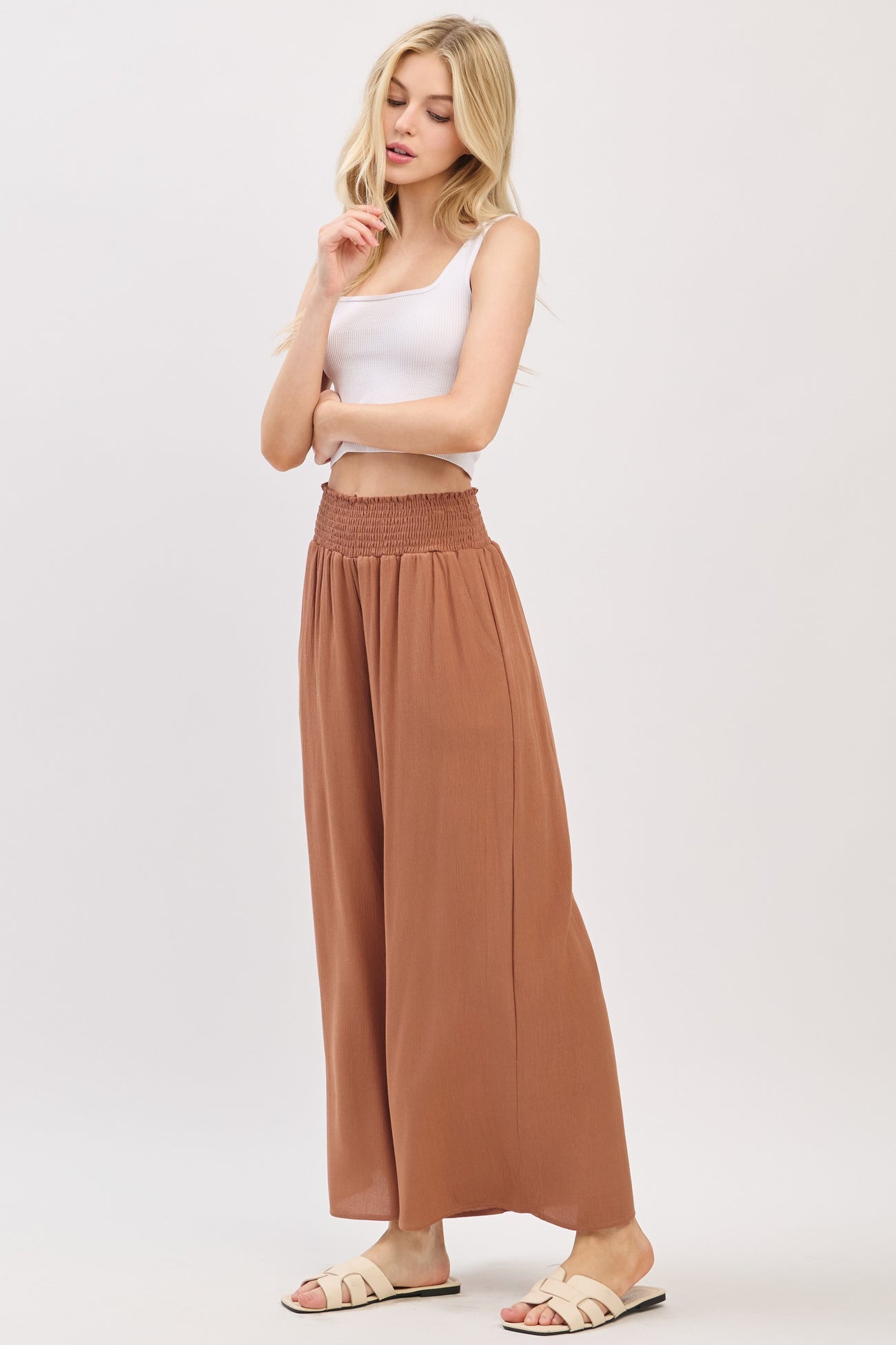woman wearing a white ribbed tank top and rust-colored wide-leg pants with a smocked waistband