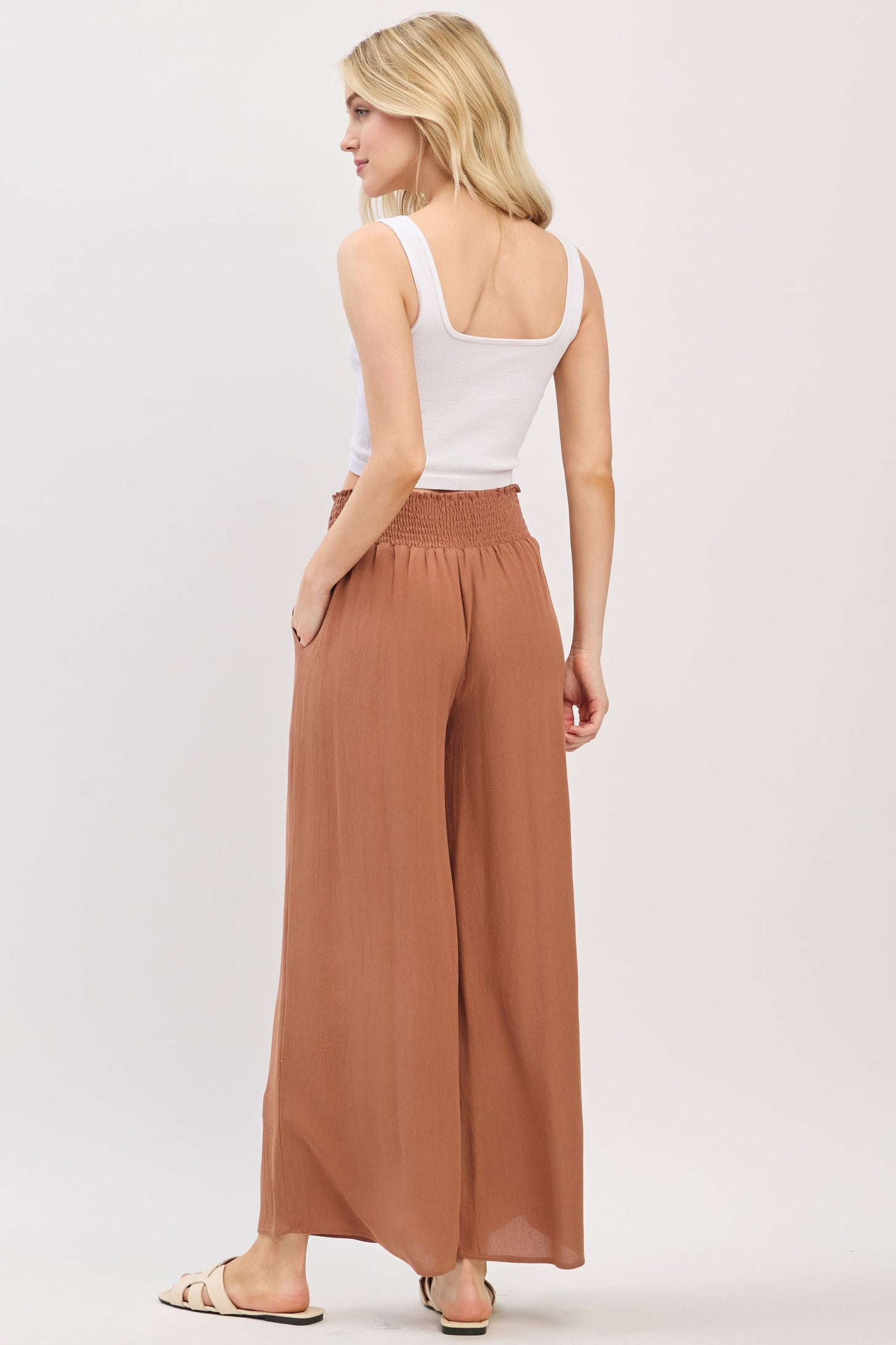 woman wearing a white sleeveless top and brown wide-leg pants, seen from the back