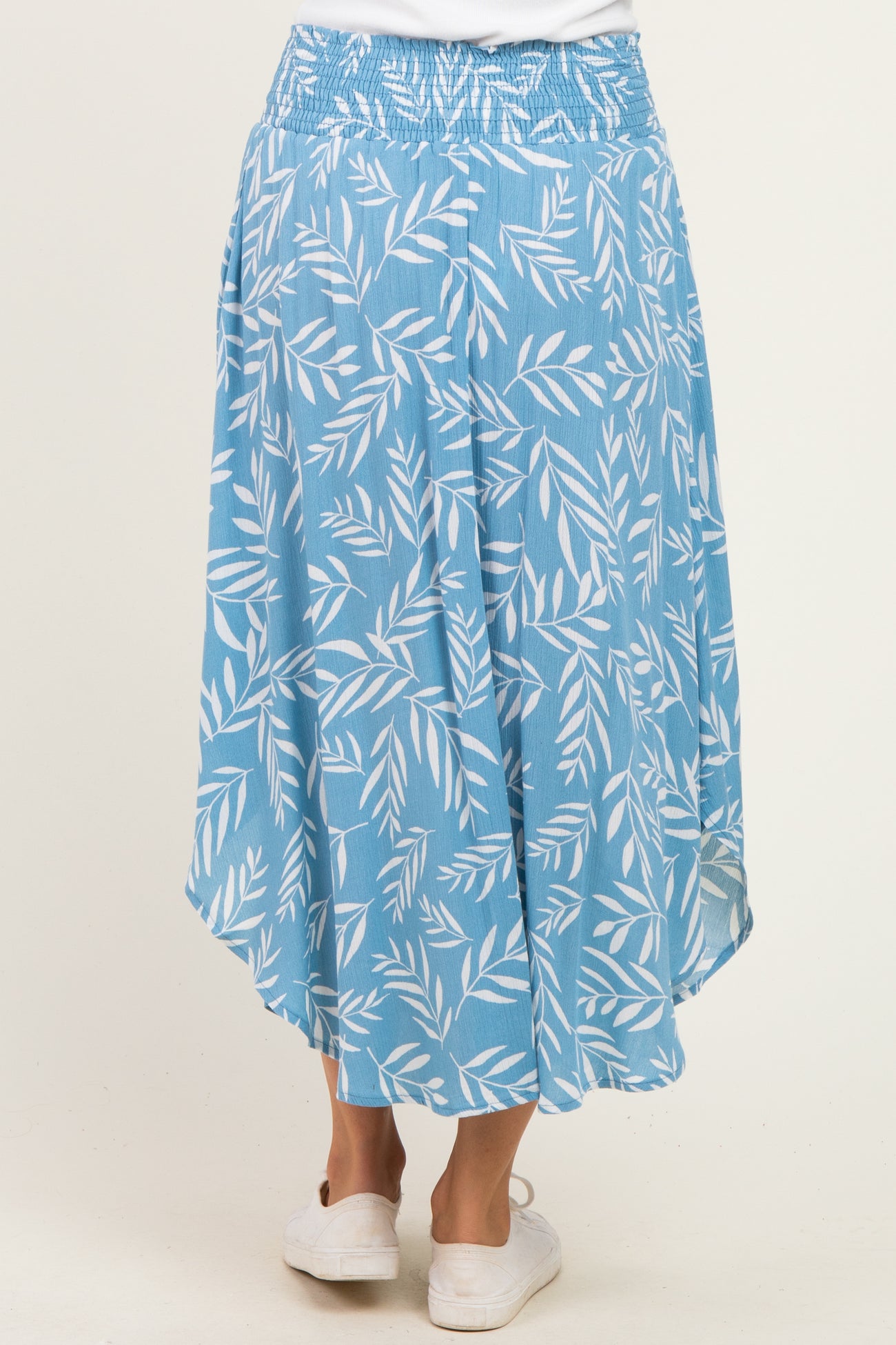 woman wearing a light blue skirt with a leaf print and an asymmetrical hemline, showing the back view