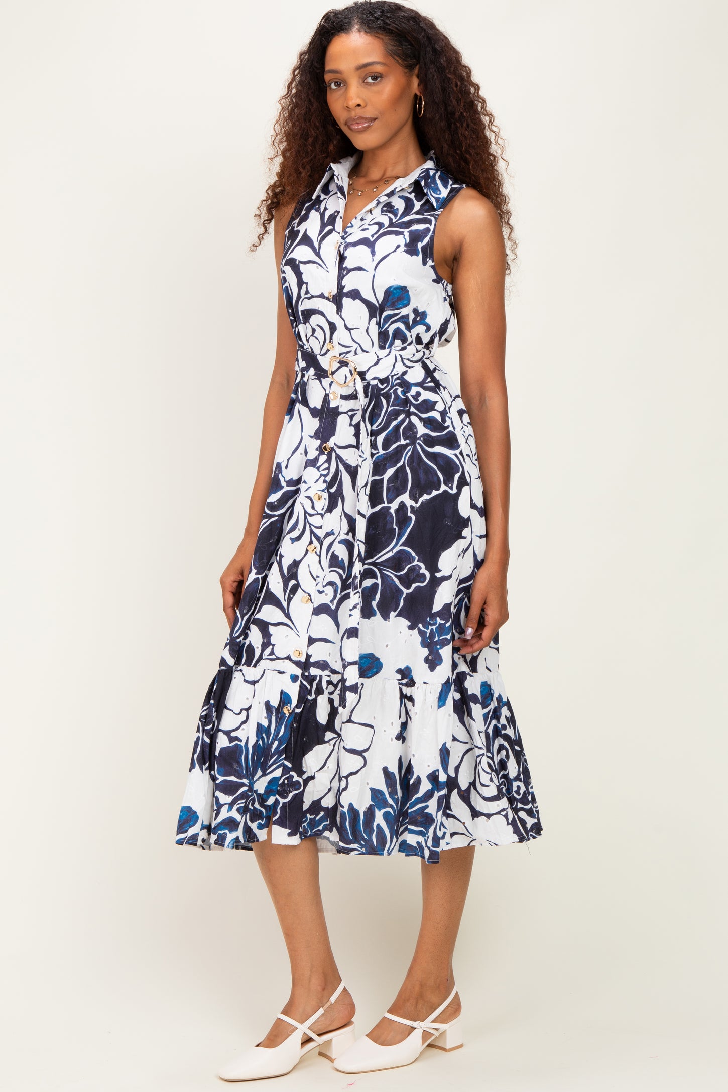 woman wearing a sleeveless navy blue and white floral dress with a belted waist and ruffled hem