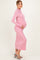 woman wearing a light pink long sleeve maternity dress with a fitted silhouette and holding her baby bump