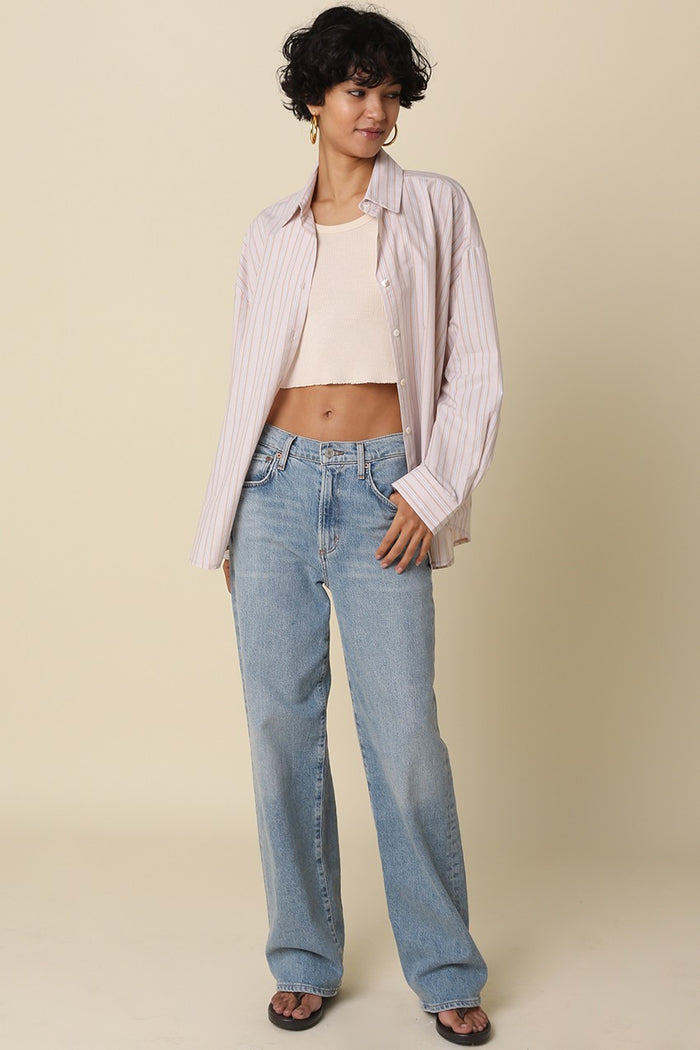 woman wearing a light pink striped oversized shirt and a fitted cropped top with high-waisted blue jeans