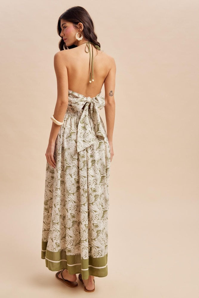 woman wearing a backless floral maxi dress with a tie at the waist and green trim, showing a natural and breezy style