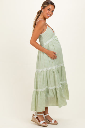 woman wearing a green maternity maxi dress with a tiered skirt and a baby bump visible, standing sideways