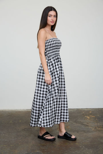 woman wearing a black and white gingham strapless maxi dress and black slide sandals