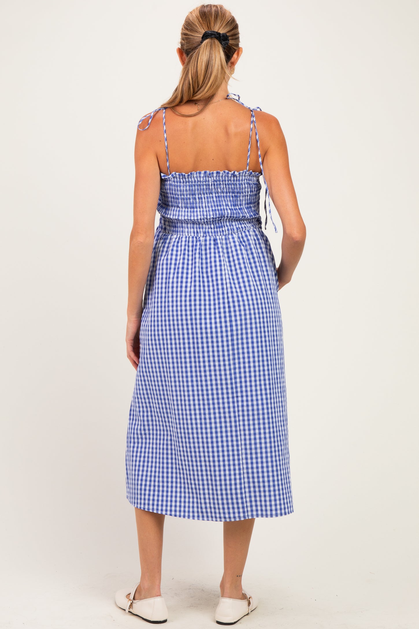 woman wearing a blue and white gingham maternity dress with adjustable straps and a smocked waist, showing her baby bump