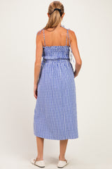 woman wearing a blue and white gingham maternity dress with adjustable straps and a smocked waist, showing her baby bump