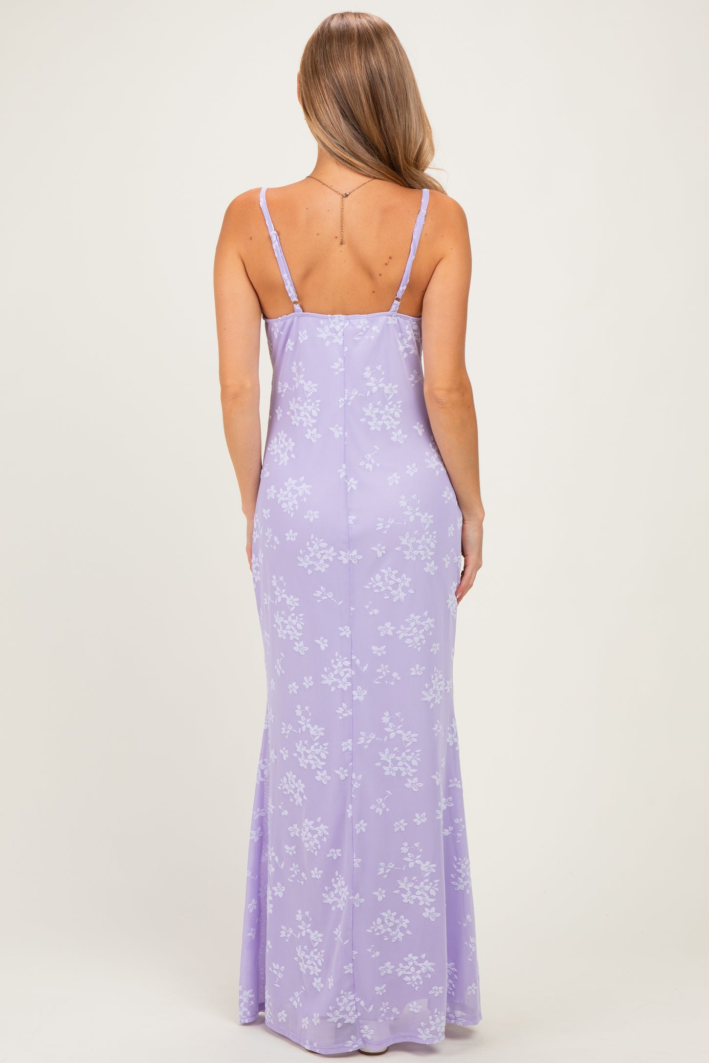 woman wearing a lavender maxi dress with a floral print and thin straps, shown from the back