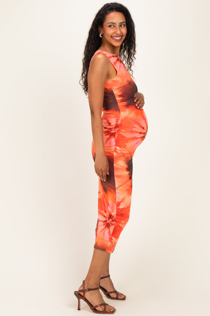 woman wearing a tie-dye orange maternity dress with a visible baby bump and brown strappy heels