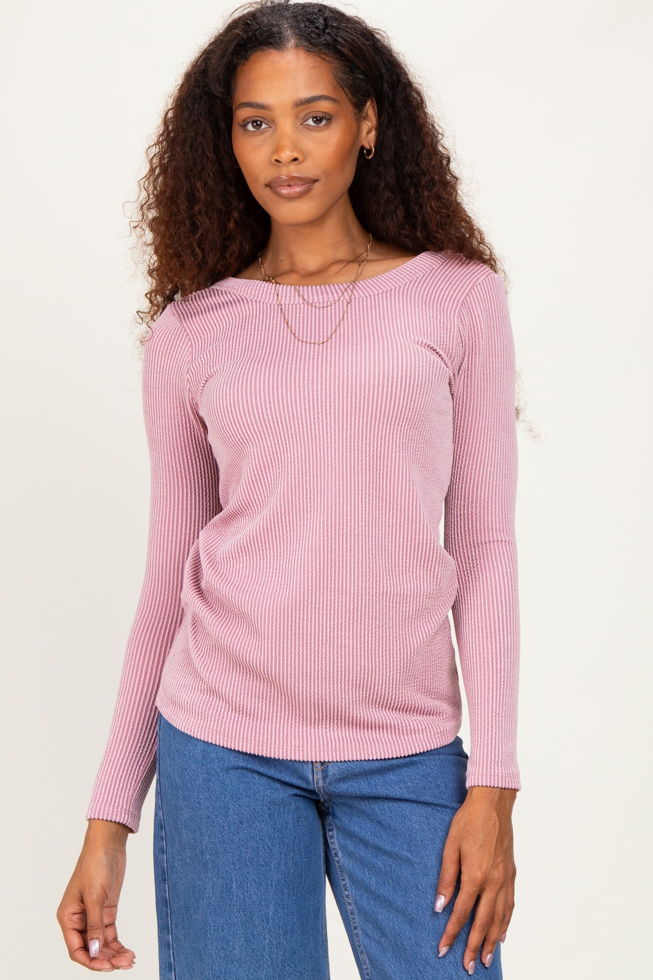 woman wearing a light pink ribbed long sleeve top with a boat neckline and stylish layered necklace paired with blue jeans