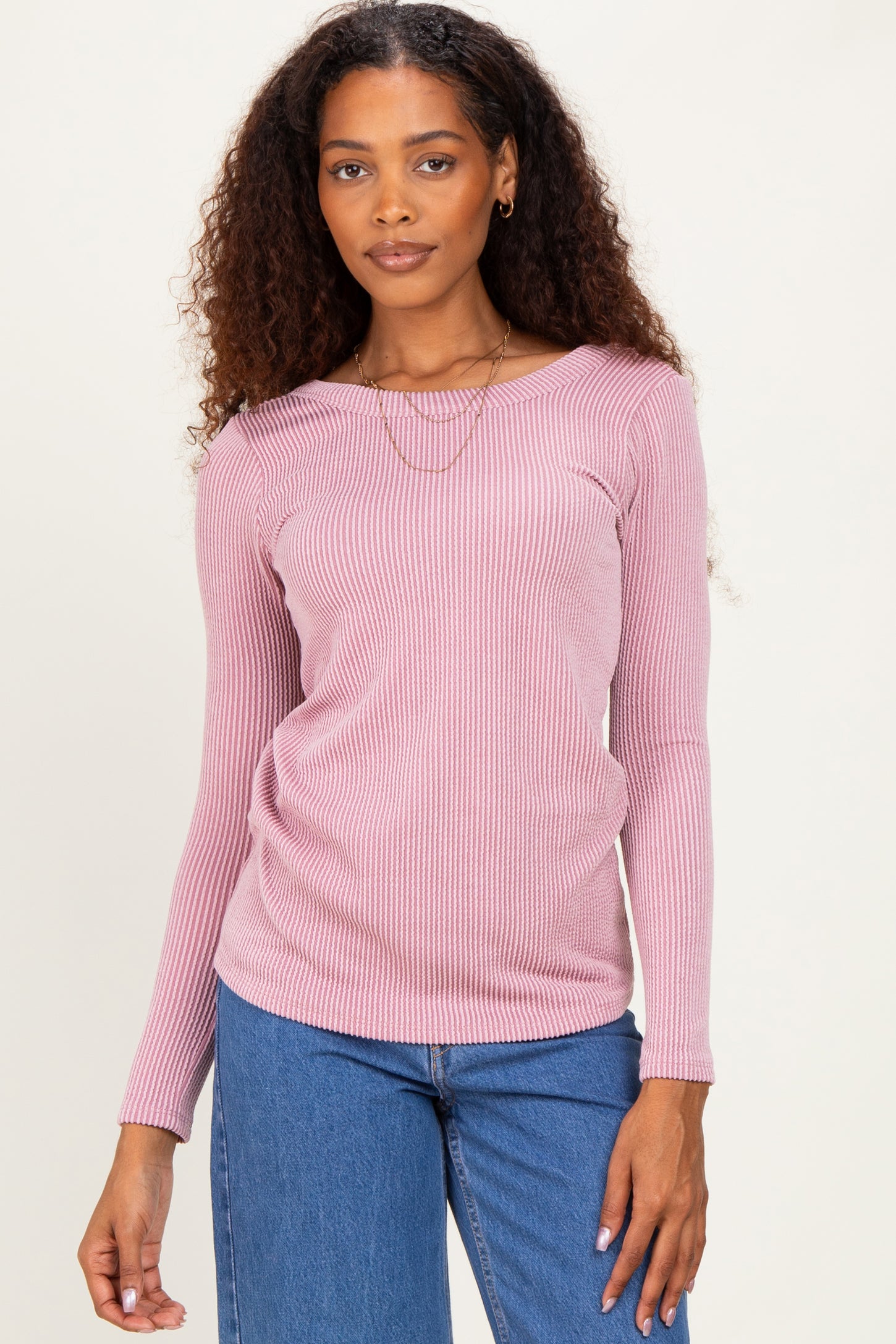 woman wearing a light pink ribbed long sleeve top with a boat neckline and stylish layered necklace paired with blue jeans