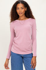 woman wearing a light pink ribbed long sleeve top with a boat neckline and stylish layered necklace paired with blue jeans