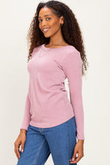 woman wearing a light pink ribbed long sleeve top paired with blue jeans, smiling and posing sideways