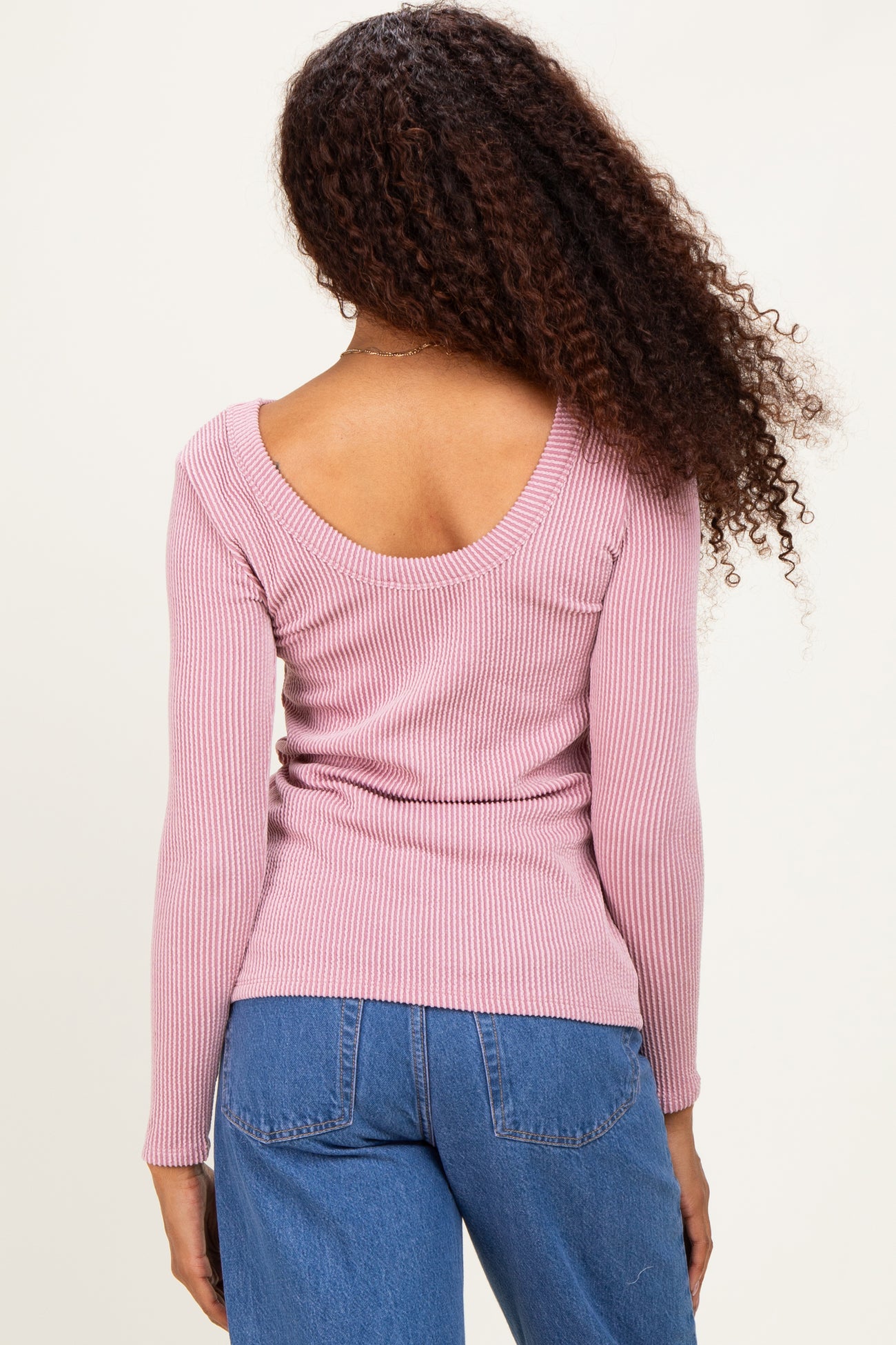 woman wearing a pink ribbed long sleeve top with a scoop back and styled with high-waisted jeans