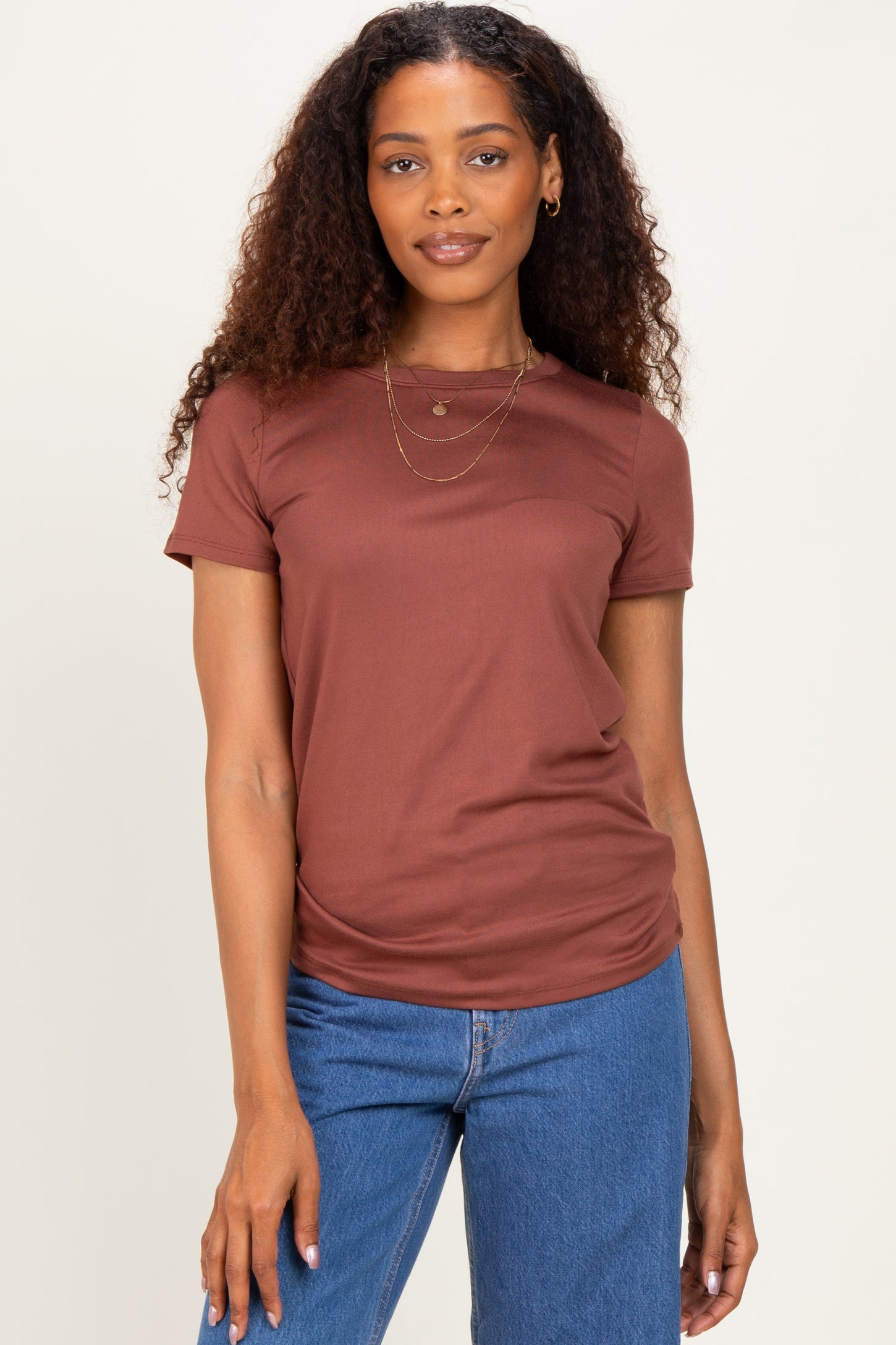 woman wearing a rust brown short sleeve top paired with blue jeans and layered necklaces