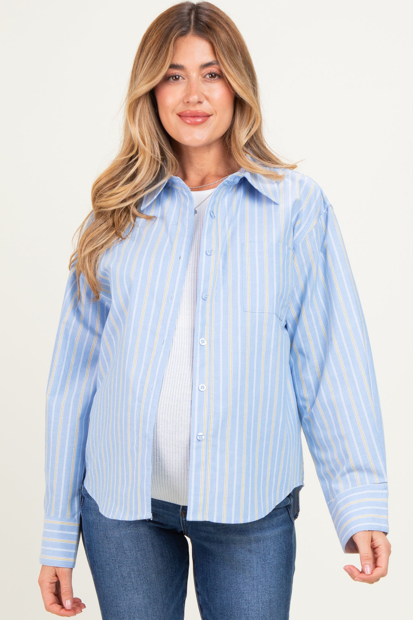 woman wearing a light blue striped maternity button-up shirt and showcasing her baby bump