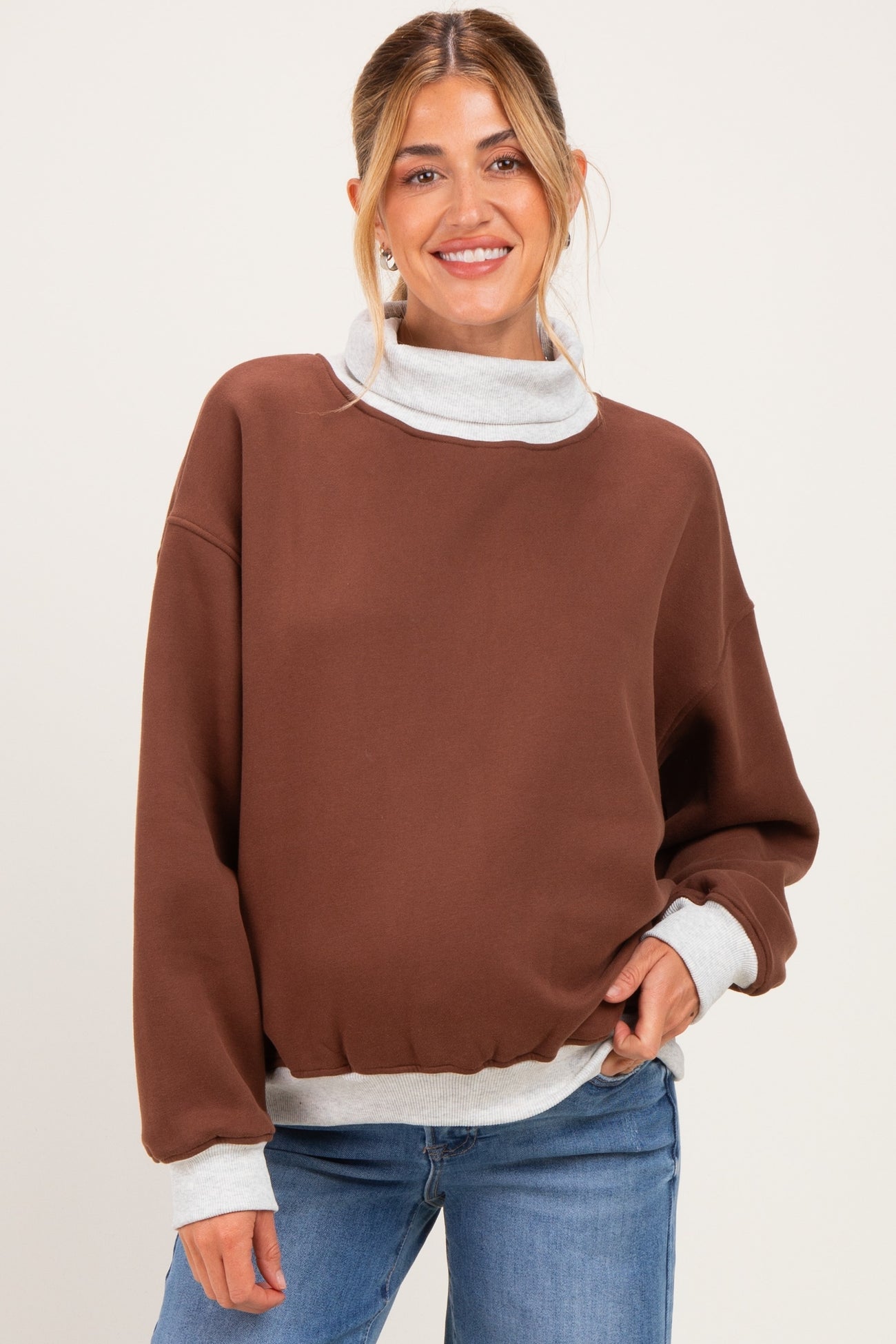 woman wearing a brown maternity sweatshirt with a light gray collar and cuffs, styled casually with jeans
