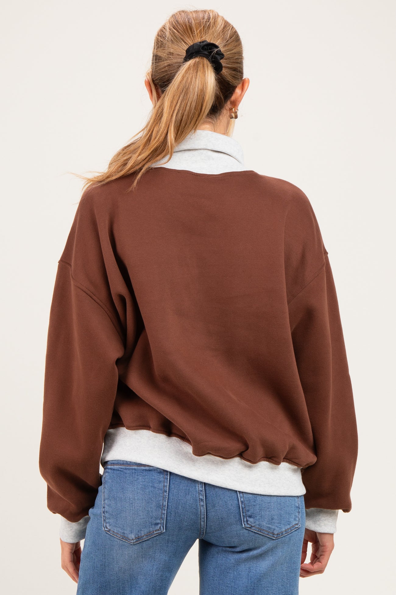 woman wearing a brown maternity sweatshirt with a gray collar and loose fit, showing her back and long sleeves