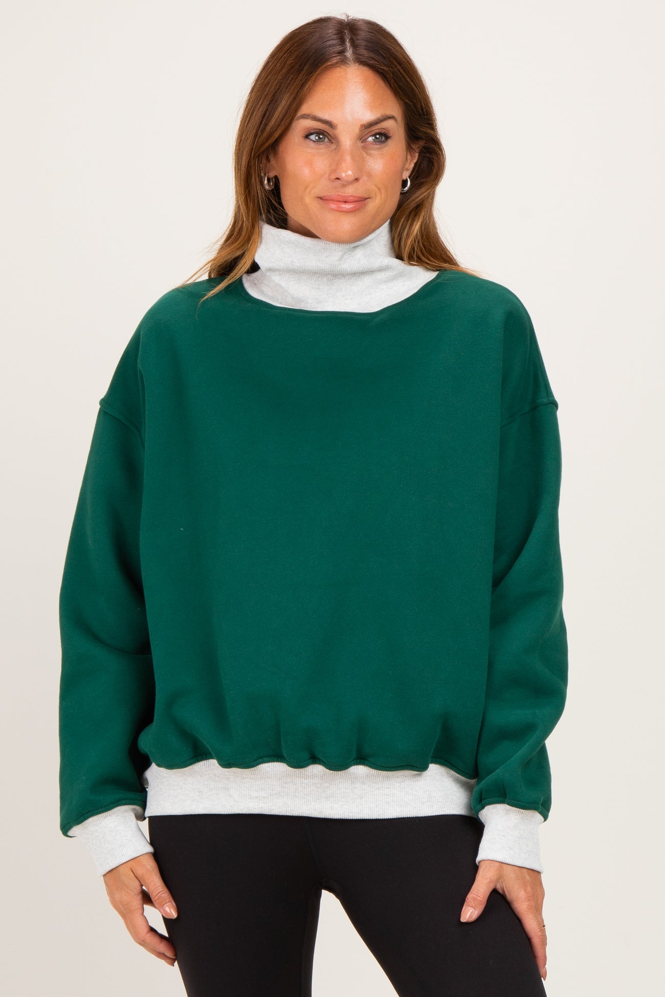 woman wearing a green oversized sweatshirt with a gray mock neck and cuffed sleeves