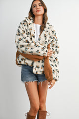 woman wearing a cream floral patterned fuzzy jacket with brown accents, paired with denim shorts and tall brown boots