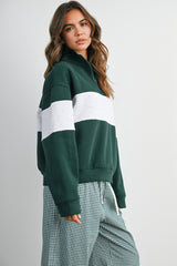 woman wearing a dark green and gray color block half-zip sweatshirt with a relaxed fit and plaid pants