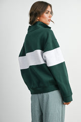 woman wearing a dark green oversized sweatshirt with a grey stripe, styled with checkered pants