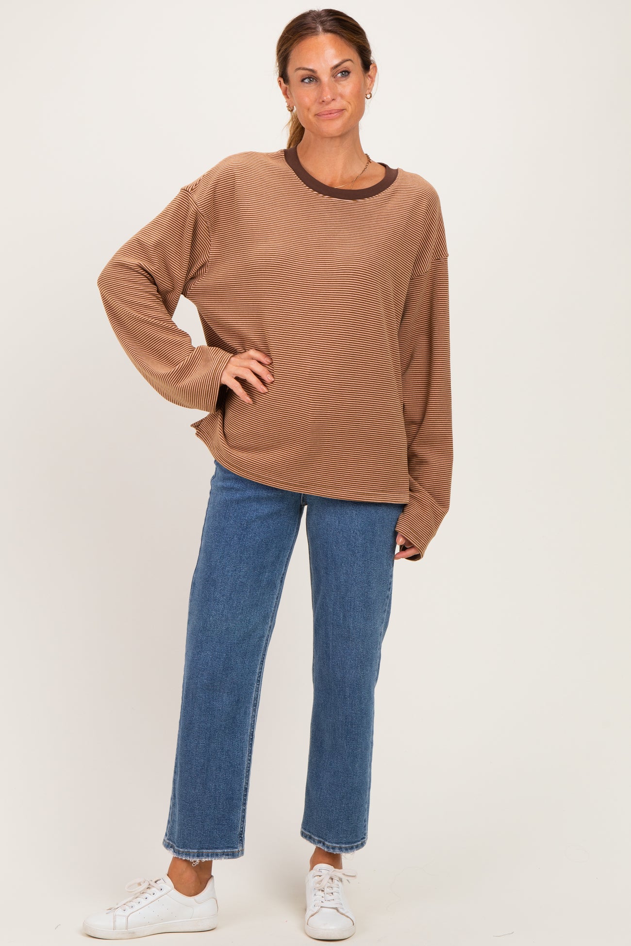 woman wearing a brown oversized sweater with a round neckline and long sleeves paired with light blue straight leg jeans
