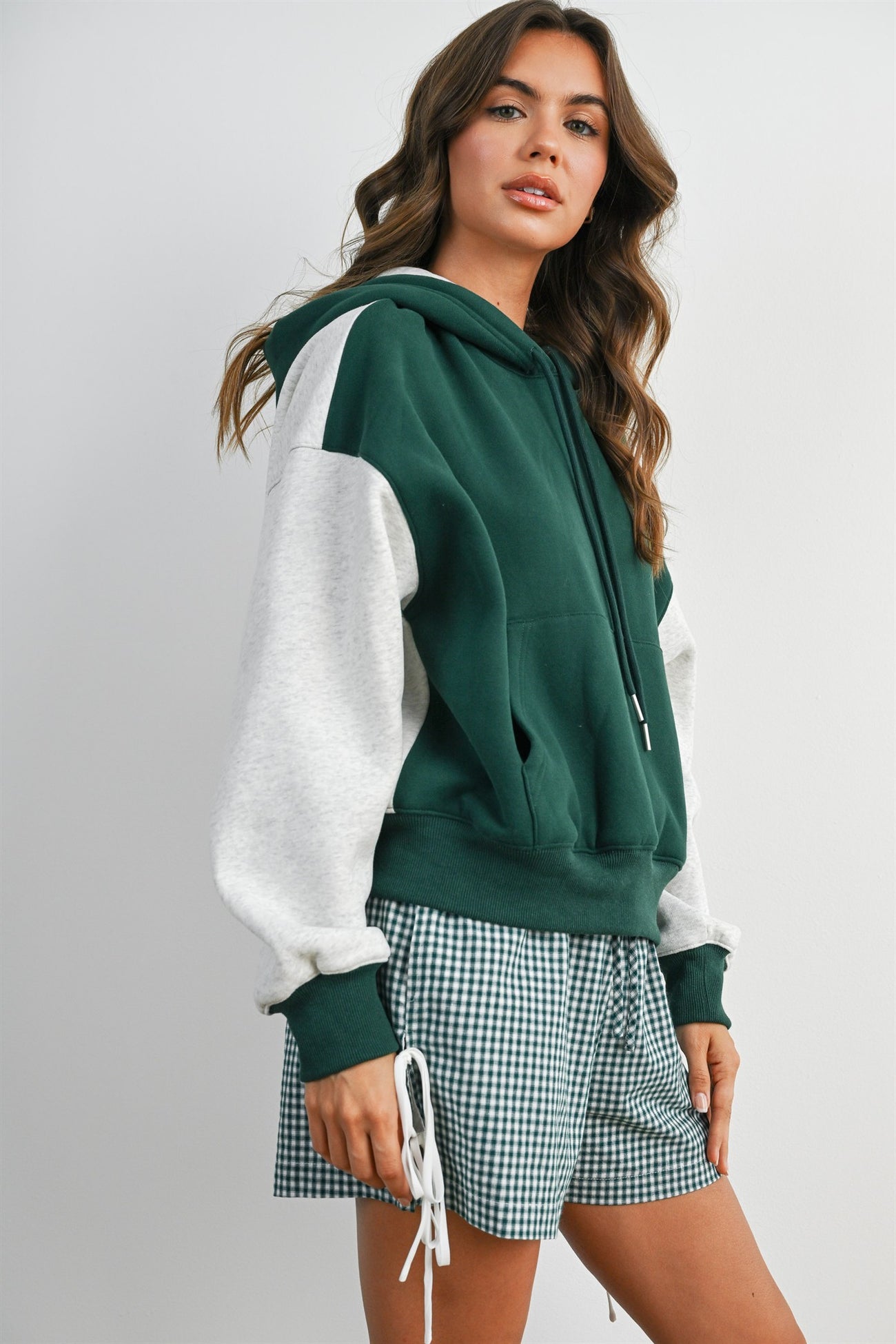 woman wearing a green and gray color block hoodie styled with plaid shorts