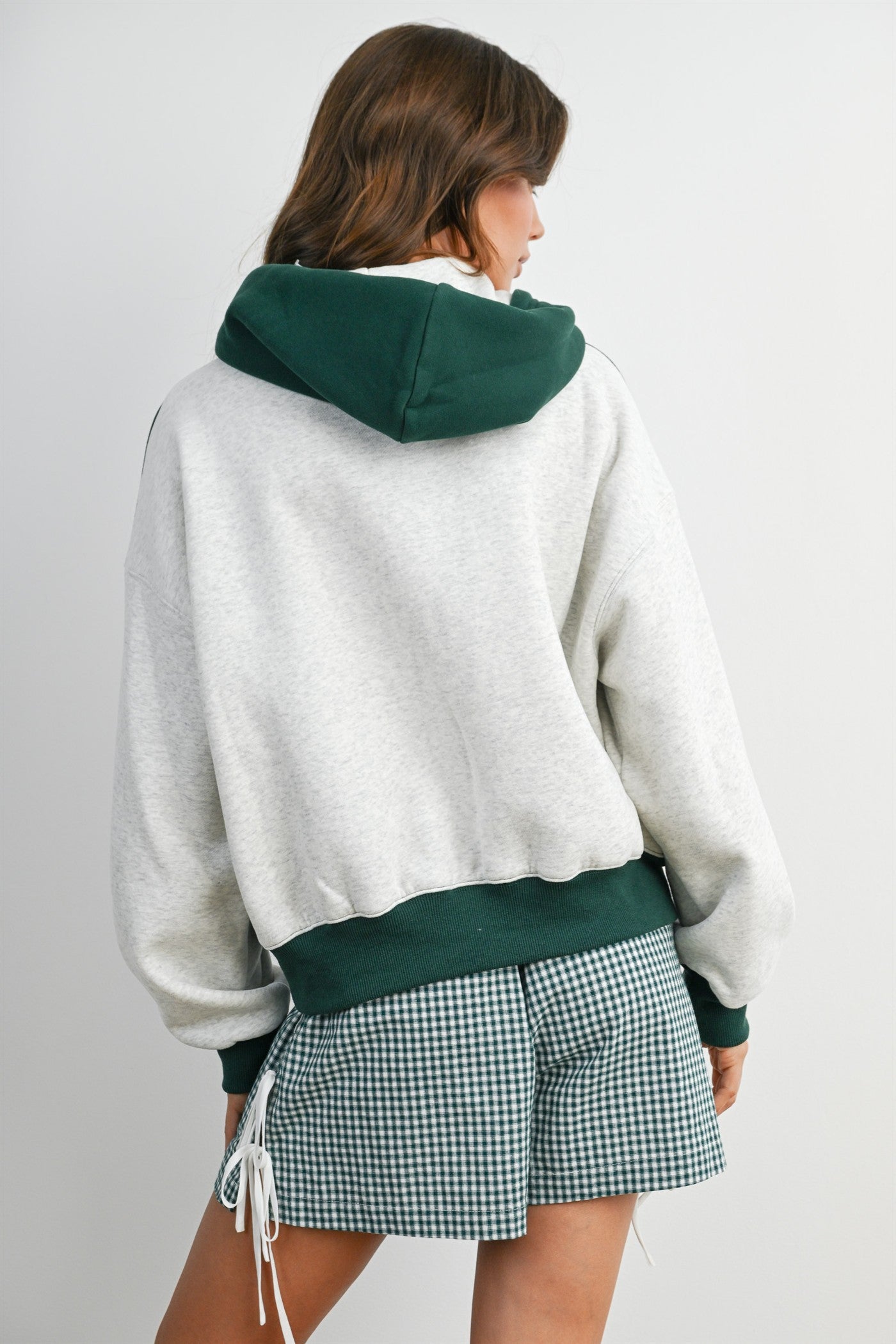 woman wearing a gray oversized hoodie with a green hood and cuffs, paired with a green plaid mini skirt