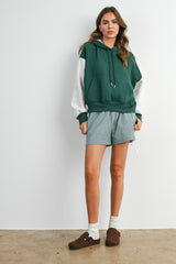 woman wearing a green and gray color-blocked hoodie with a kangaroo pocket and checkered shorts