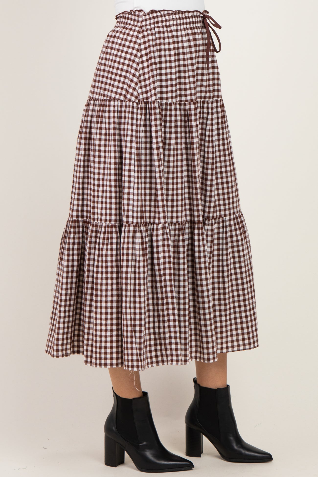 woman wearing a brown and white gingham tiered maxi skirt with a drawstring waist and black ankle boots