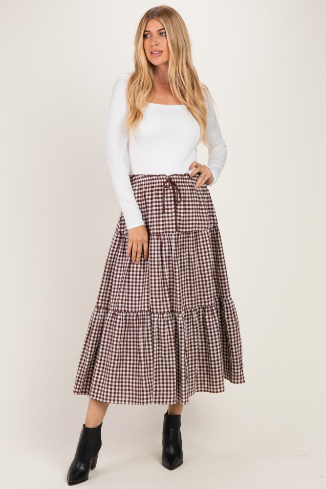 woman wearing a white long sleeve top and a brown and white checkered maxi skirt with a tie waist