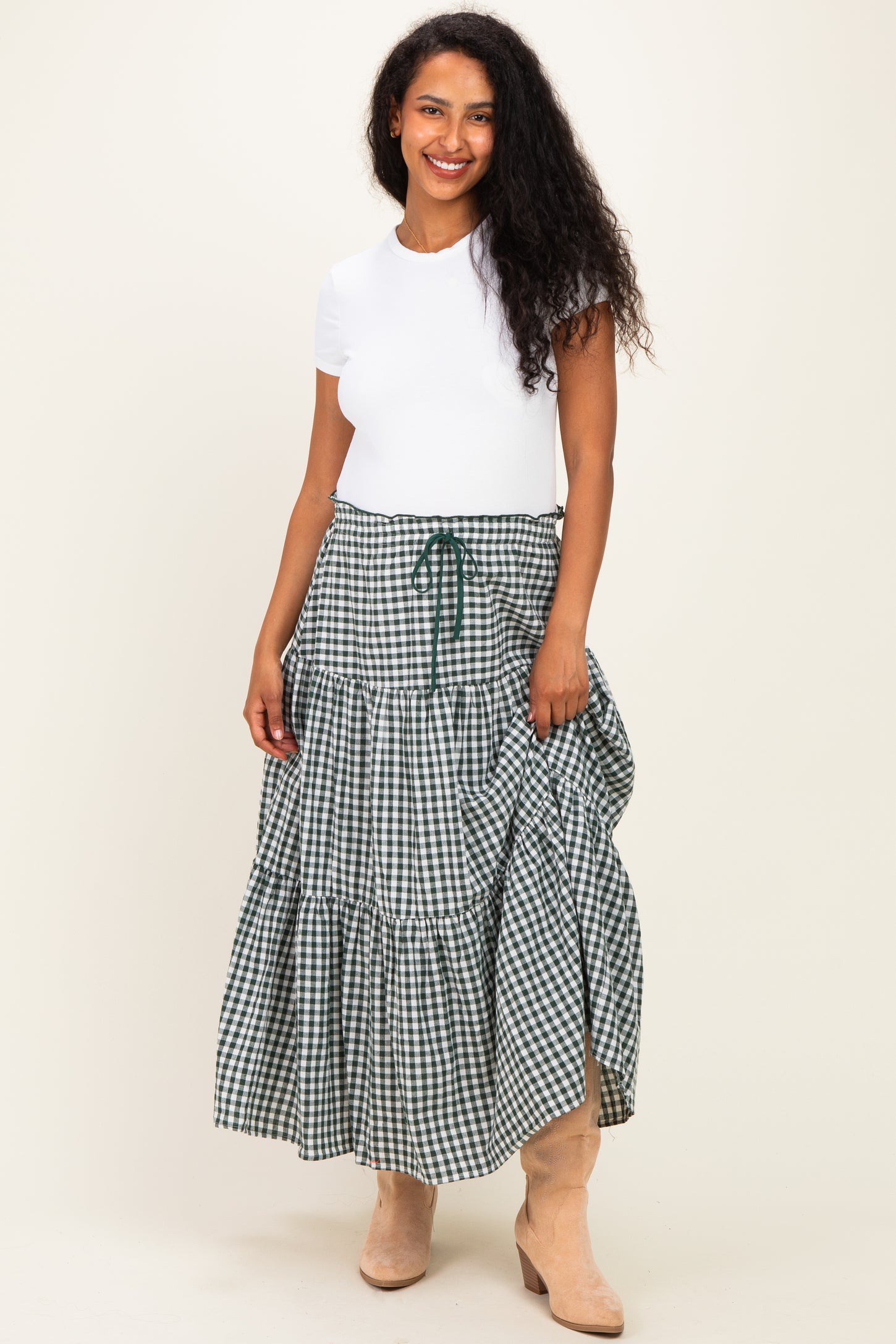 woman wearing a white short sleeve top and a green gingham print maternity skirt with a tiered design and drawstring waist