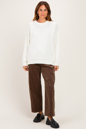 woman wearing an oversized white knit sweater and brown wide-leg corduroy pants with black slip-on shoes