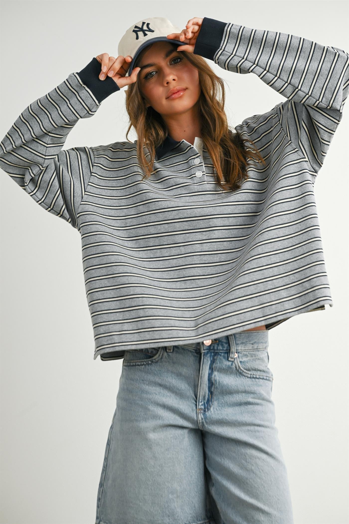 woman wearing a gray and navy striped cropped polo sweatshirt with long sleeves and light blue high-waisted jeans