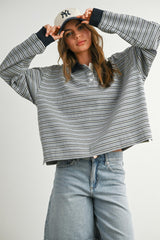 woman wearing a gray and navy striped cropped polo sweatshirt with long sleeves and light blue high-waisted jeans