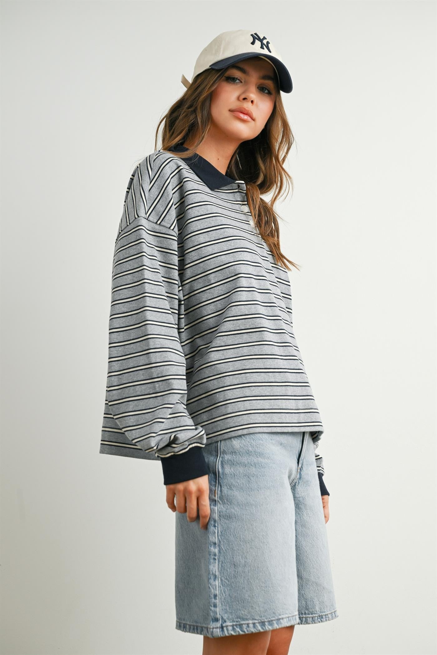 woman wearing a gray striped long sleeve top with navy collar and a cap, paired with denim shorts